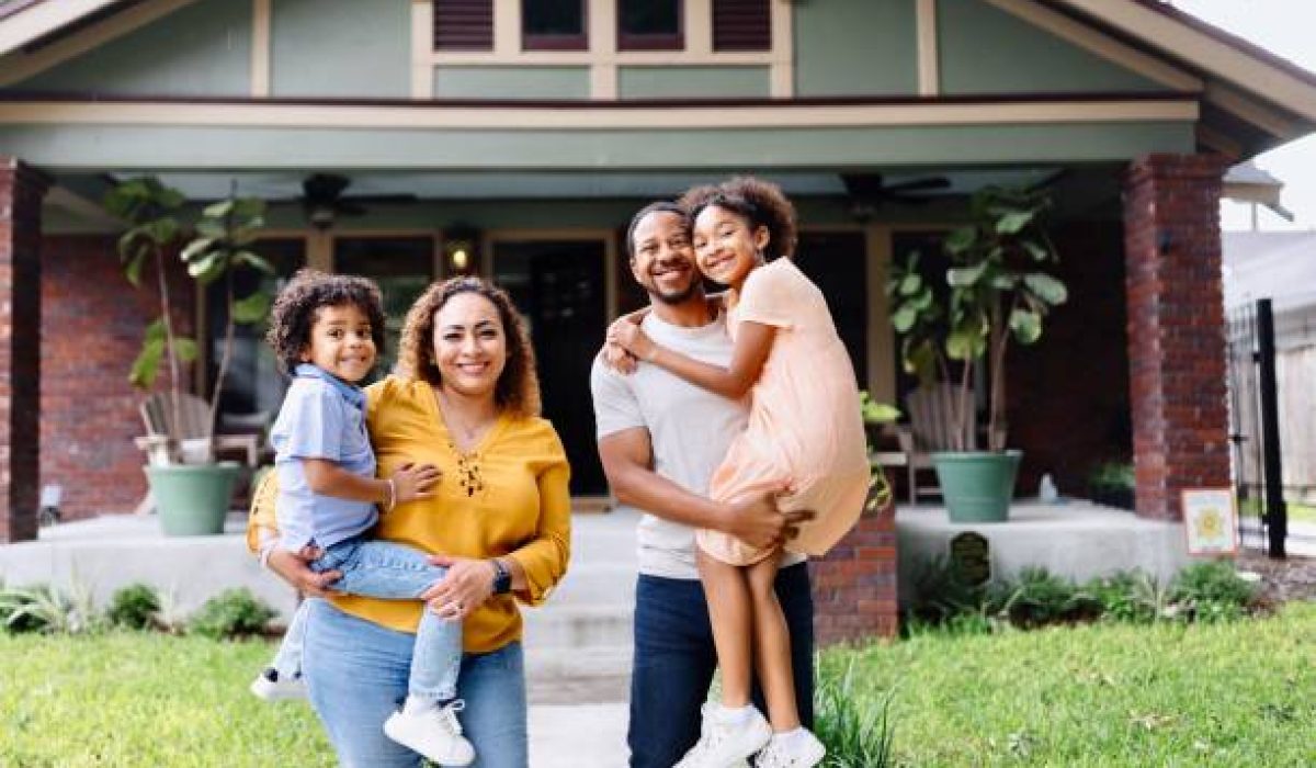 Portrait of multiracial parents holding their kids in front of the house